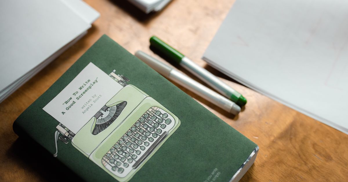 Book with vintage typewriter cover and pens on a wooden desk for screenplay writing.